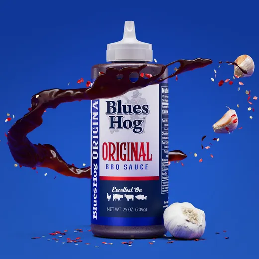 A stylized bottle of Blues Hog Original BBQ sauce on a blue background with liquid splashing.