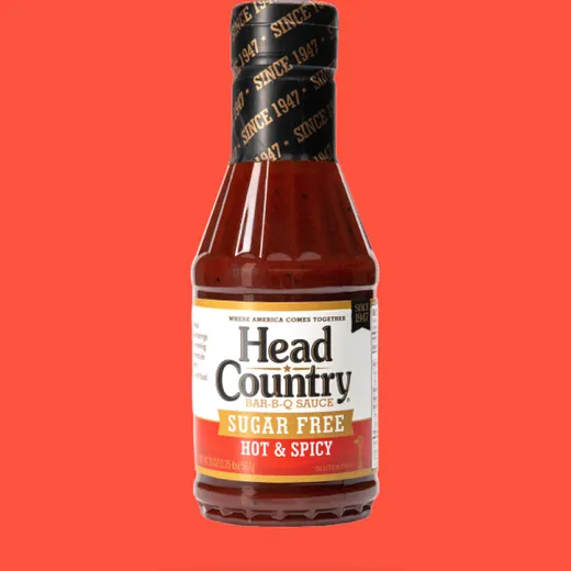 A full bottle of Head Country Sugar Free Hot and Spicy BBQ Sauce against an orange background.