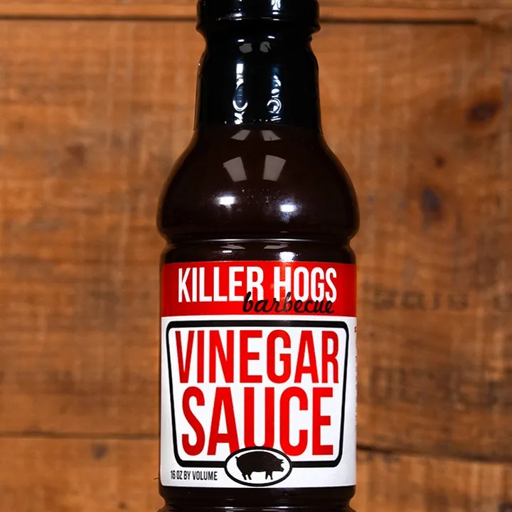 A bottle of Killer Hogs Vinegar Sauce set against a wood background.