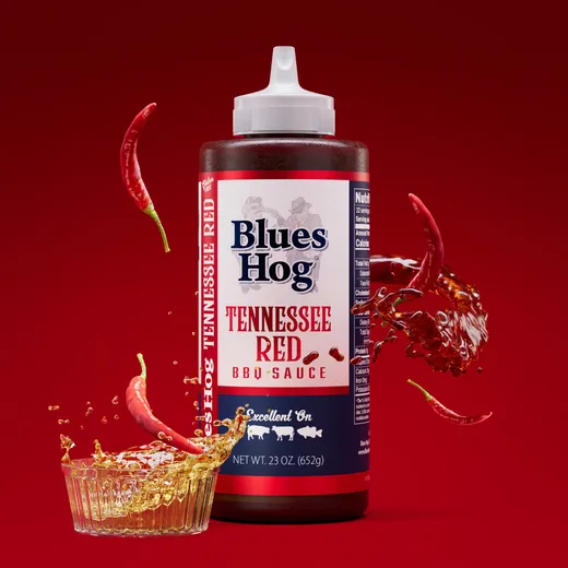 Blues Hog Tennessee Red barbecue sauce bottle on a red background with chili peppers and sauce flying around it.