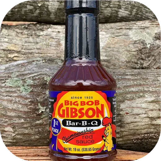 A single bottle of Big Bob Gibson Championship red sauce centered on a wood log background.