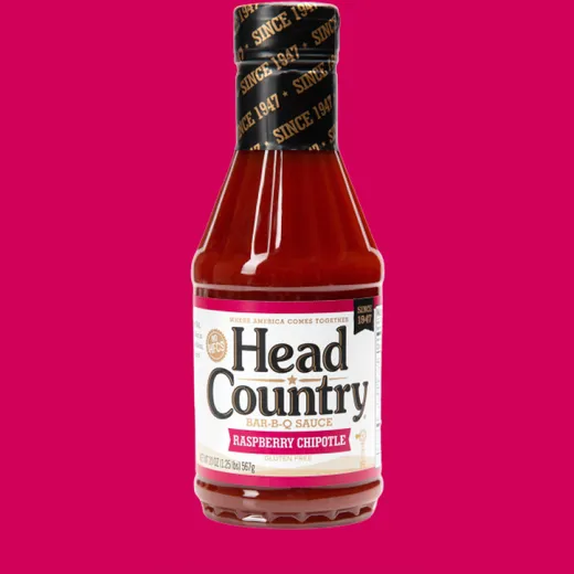 A bottle of Head Country Raspberry Chipotle BBQ sauce against a pink background.