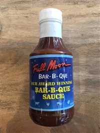 A bottle of Full Moon Award Winning Bar-B-Que Sauce standing on a wooden surface.